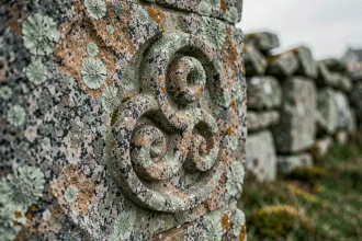 Sculpture de triskel breton gravée dans une pierre de granit ancienne recouverte de lichen, symbole celtique de protection et d'identité bretonne